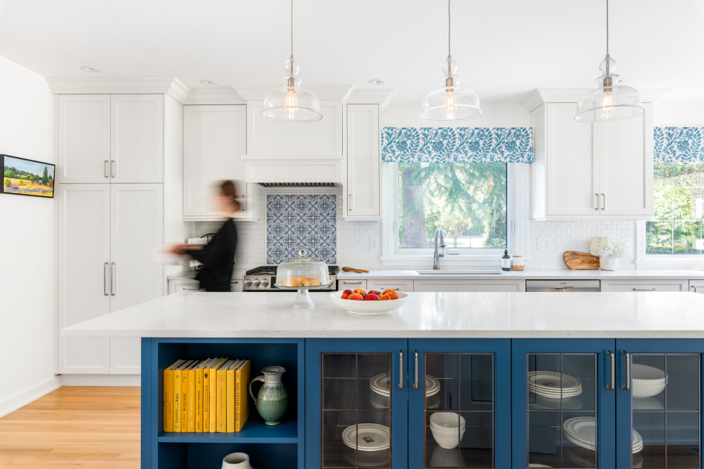 Example of a mid-sized classic l-shaped light wood floor and yellow floor enclosed kitchen design in Vancouver with an undermount sink, shaker cabinets, white cabinets, quartz countertops, white backsplash, ceramic backsplash, stainless steel appliances, an island and white countertops