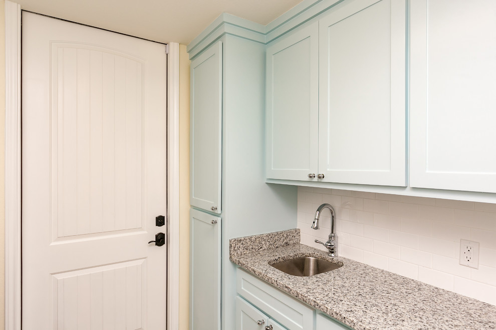 Mid-sized beach style single-wall utility room in Austin with an undermount sink, shaker cabinets, blue cabinets, granite benchtops, yellow walls, a side-by-side washer and dryer and porcelain floors.