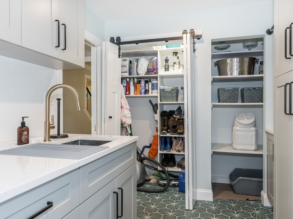 Design ideas for a mid-sized galley utility room in New York with an undermount sink, shaker cabinets, grey cabinets, quartz benchtops, white splashback, ceramic splashback, blue walls, porcelain floors, a stacked washer and dryer, blue floor and white benchtop.