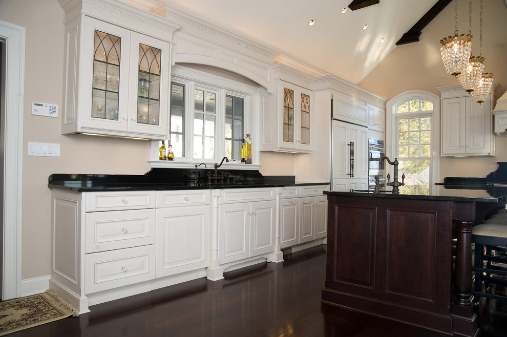 Photo of a large traditional l-shaped eat-in kitchen in Bridgeport with an undermount sink, raised-panel cabinets, white cabinets, granite benchtops, panelled appliances, dark hardwood floors, with island and brown floor.