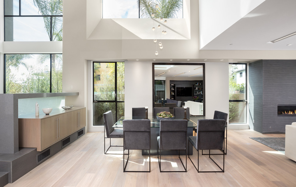 Inspiration for a contemporary open plan dining in Los Angeles with white walls, light hardwood floors, a standard fireplace, a tile fireplace surround and beige floor.