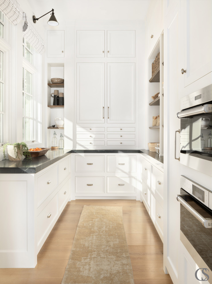 Example of an u-shaped light wood floor kitchen pantry design in Salt Lake City with shaker cabinets, white cabinets, paneled appliances and black countertops