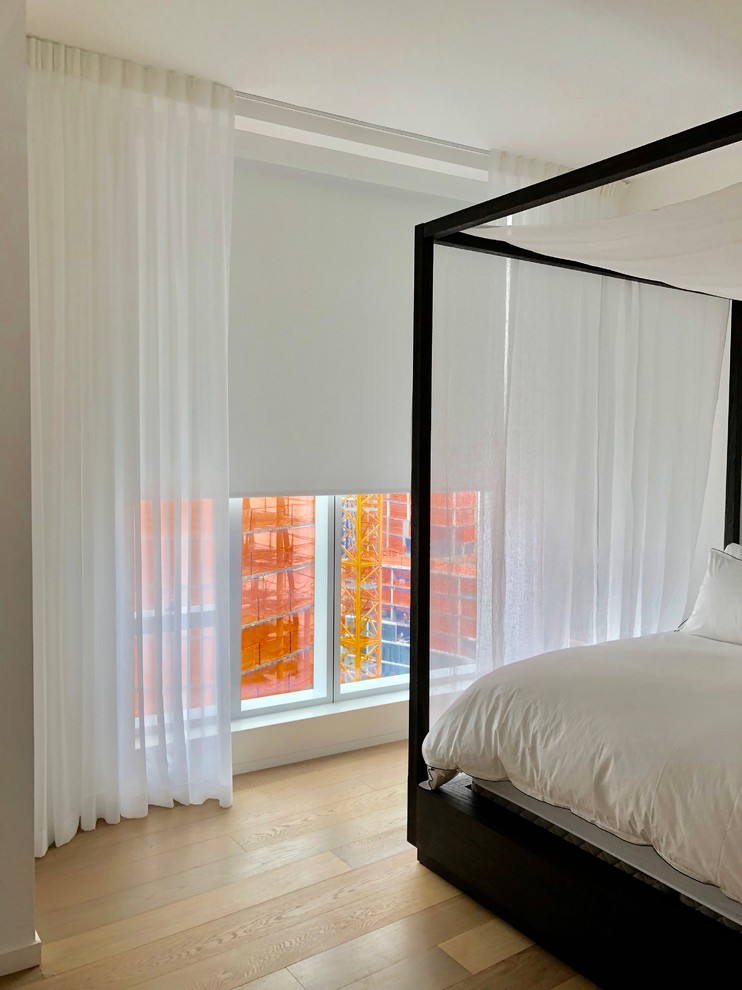 Photo of a mid-sized modern master bedroom in New York with white walls and light hardwood floors.