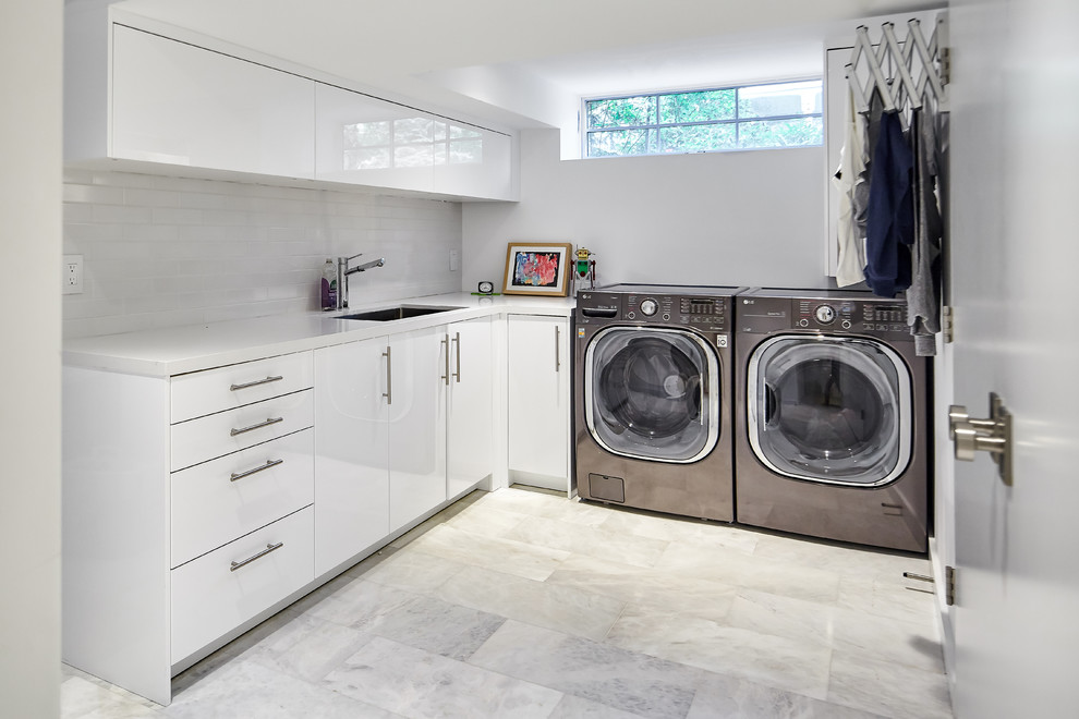 This is an example of a large contemporary l-shaped separated utility room in Toronto with a submerged sink, flat-panel cabinets, white cabinets, engineered stone countertops, white splashback, ceramic splashback, white walls, porcelain flooring, a side by side washer and dryer, white floors and white worktops.