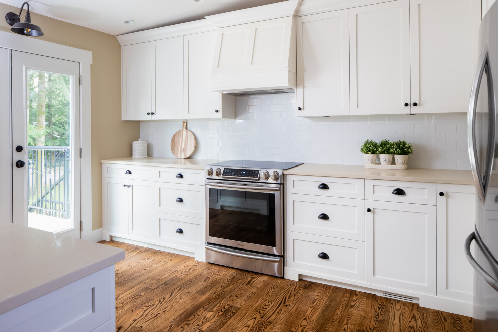 Inspiration for a large rustic l-shaped medium tone wood floor and brown floor eat-in kitchen remodel in Vancouver with a farmhouse sink, shaker cabinets, white cabinets, quartzite countertops, white backsplash, subway tile backsplash, stainless steel appliances, an island and white countertops