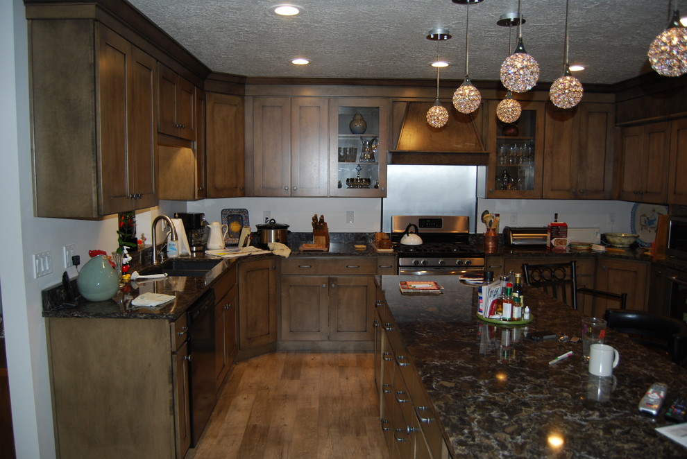 Inspiration for a large transitional u-shaped vinyl floor and brown floor eat-in kitchen remodel with recessed-panel cabinets, brown cabinets, black backsplash, stainless steel appliances, an island, quartz countertops and a double-bowl sink