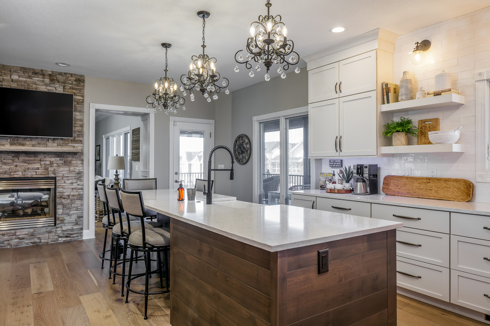 Eat-in kitchen - u-shaped brown floor eat-in kitchen idea with a farmhouse sink, shaker cabinets, white cabinets, quartz countertops, white backsplash, subway tile backsplash, stainless steel appliances, an island and white countertops