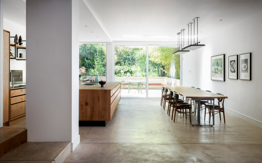 This is an example of a large contemporary single-wall eat-in kitchen in London with a drop-in sink, flat-panel cabinets, wood benchtops, metal splashback, stainless steel appliances, concrete floors, with island, recessed and medium wood cabinets.