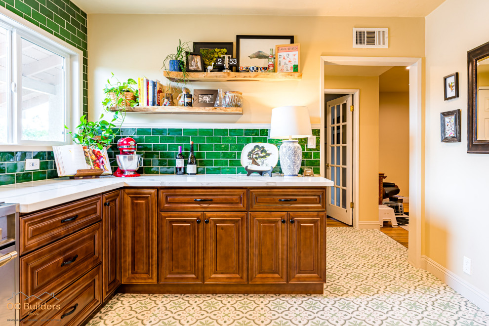オレンジカウンティにあるお手頃価格の中くらいなヴィクトリアン調のおしゃれなキッチン (エプロンフロントシンク、レイズドパネル扉のキャビネット、濃色木目調キャビネット、珪岩カウンター、緑のキッチンパネル、サブウェイタイルのキッチンパネル、シルバーの調理設備、セラミックタイルの床、ベージュの床、白いキッチンカウンター) の写真