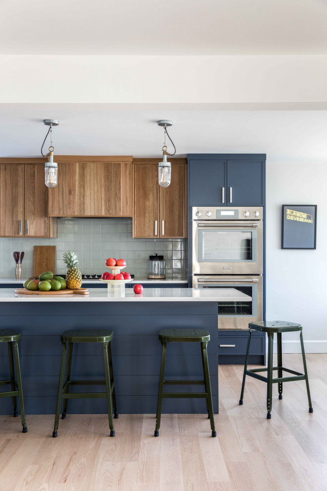 Design ideas for a large midcentury l-shaped eat-in kitchen in Portland Maine with shaker cabinets, blue cabinets, quartz benchtops, grey splashback, ceramic splashback, stainless steel appliances, light hardwood floors, with island and grey benchtop.