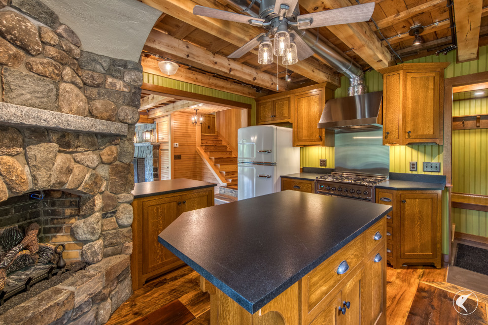 Example of a mountain style medium tone wood floor and exposed beam kitchen design with an undermount sink, shaker cabinets, granite countertops, black backsplash, granite backsplash, stainless steel appliances, an island and black countertops