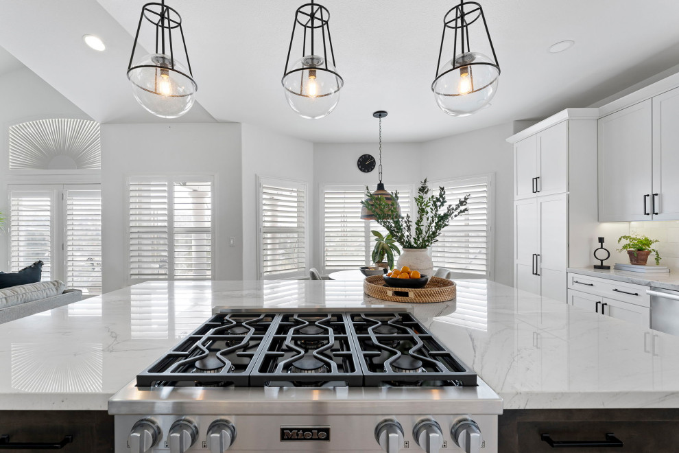 Example of a transitional vinyl floor and brown floor kitchen design with a farmhouse sink, shaker cabinets, white cabinets, quartzite countertops, white backsplash and stainless steel appliances