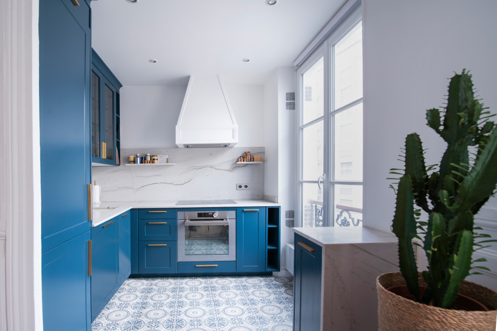 This is an example of a small l-shaped open plan kitchen in Paris with an undermount sink, blue cabinets, marble benchtops, white splashback, marble splashback, stainless steel appliances, cement tiles, blue floor and white benchtop.