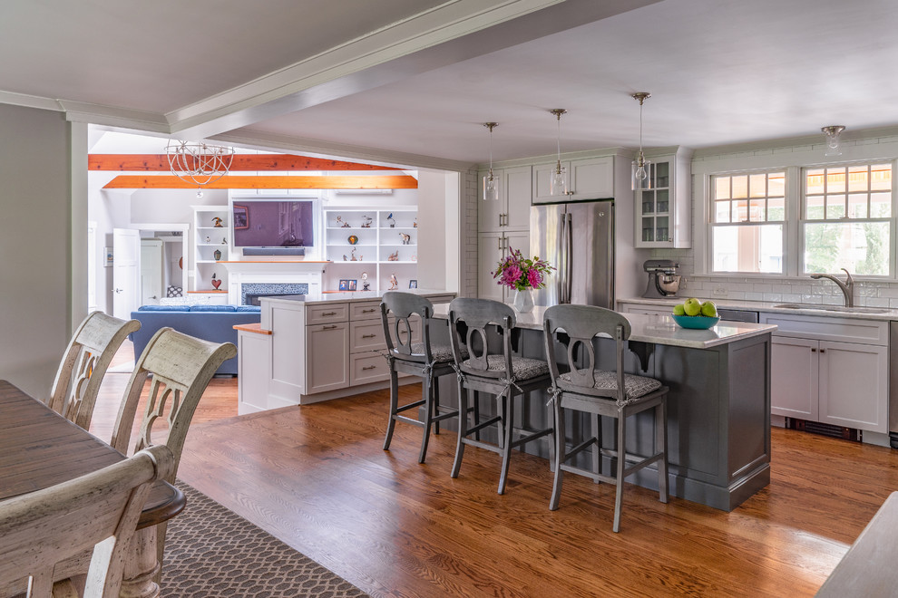 Mid-sized transitional l-shaped eat-in kitchen in Boston with an undermount sink, shaker cabinets, white cabinets, quartz benchtops, white splashback, ceramic splashback, stainless steel appliances, medium hardwood floors, with island and white benchtop.