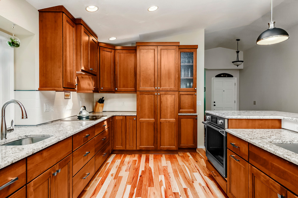 Design ideas for a traditional galley eat-in kitchen in Boise with recessed-panel cabinets, medium wood cabinets, granite benchtops, stainless steel appliances, light hardwood floors and with island.