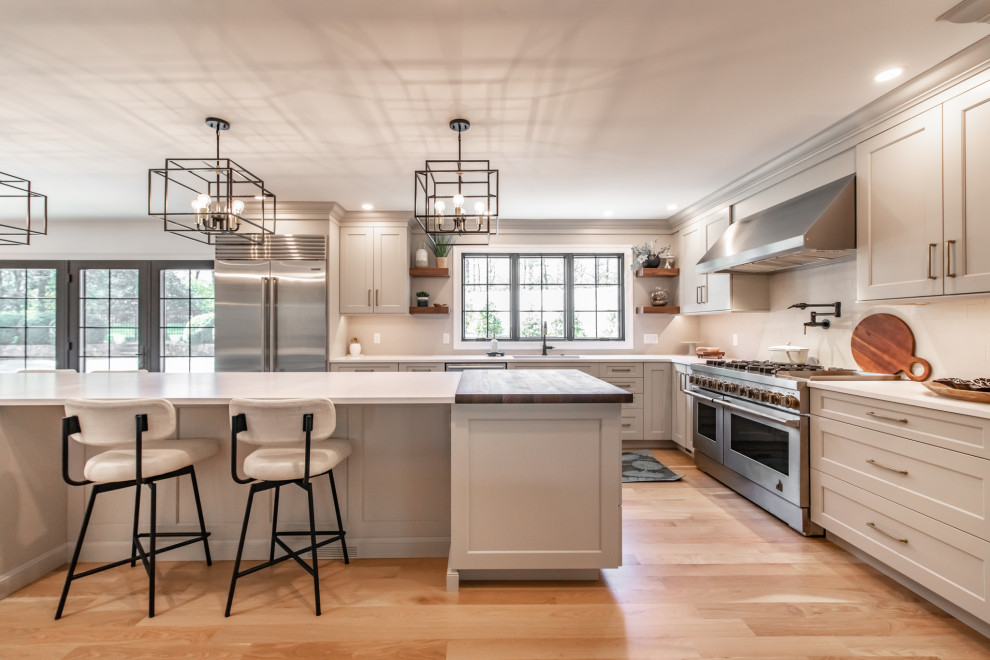 Photo of a large transitional l-shaped kitchen in Philadelphia with an undermount sink, recessed-panel cabinets, white cabinets, quartz benchtops, beige splashback, porcelain splashback, stainless steel appliances, medium hardwood floors, with island, beige floor and white benchtop.