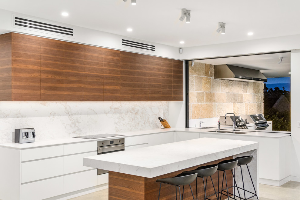 Design ideas for a contemporary l-shaped kitchen in Sydney with a double-bowl sink, flat-panel cabinets, medium wood cabinets, white splashback, stone slab splashback, stainless steel appliances, with island, beige floor and white benchtop.