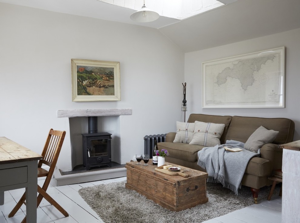 Photo of a mid-sized country formal enclosed living room in Cornwall with white walls, painted wood floors, a wood stove, a plaster fireplace surround and white floor.