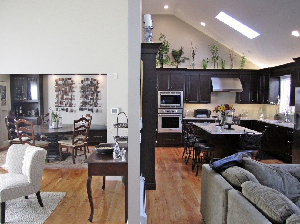 Example of a large transitional l-shaped light wood floor eat-in kitchen design with shaker cabinets, black cabinets, marble countertops, white backsplash, subway tile backsplash, stainless steel appliances and an island