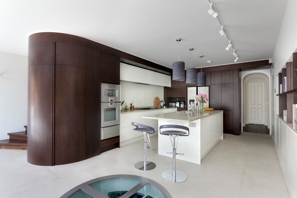 Large contemporary l-shaped eat-in kitchen in London with flat-panel cabinets, white cabinets, white splashback, a drop-in sink, solid surface benchtops, glass sheet splashback, stainless steel appliances, limestone floors, with island, grey floor and grey benchtop.