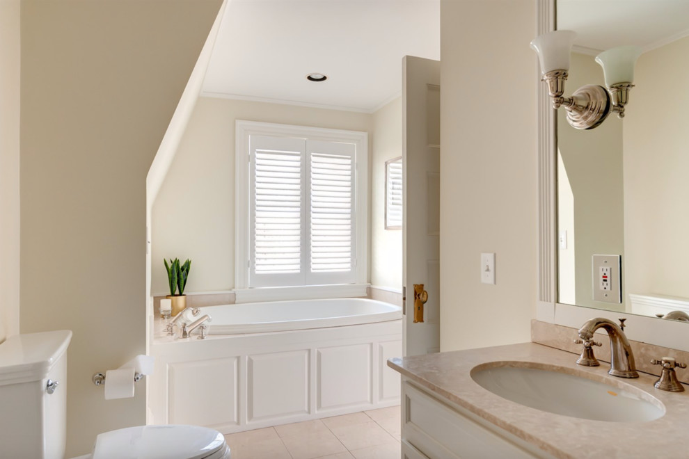 Photo of an expansive transitional master bathroom in Boston with raised-panel cabinets, white cabinets, an alcove tub, a two-piece toilet, beige walls, ceramic floors, a drop-in sink, solid surface benchtops and beige floor.