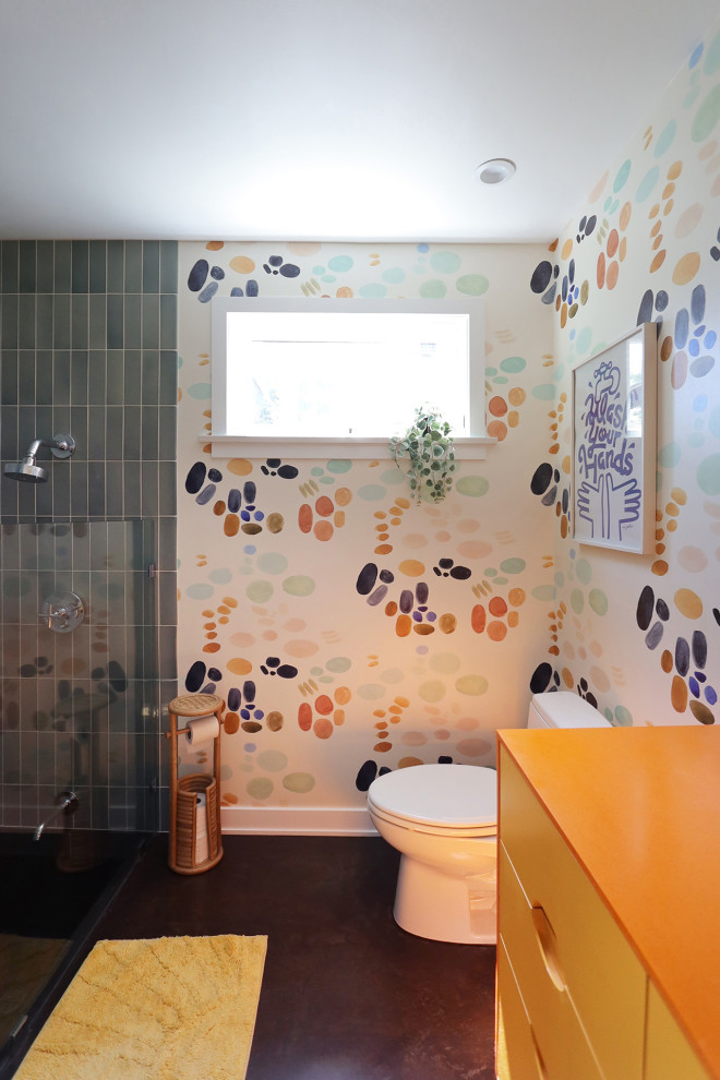Inredning av ett eklektiskt mellanstort orange oranget en-suite badrum, med släta luckor, gula skåp, en dusch i en alkov, en toalettstol med hel cisternkåpa, blå kakel, keramikplattor, flerfärgade väggar, betonggolv, ett undermonterad handfat, bänkskiva i akrylsten, rött golv och dusch med gångjärnsdörr