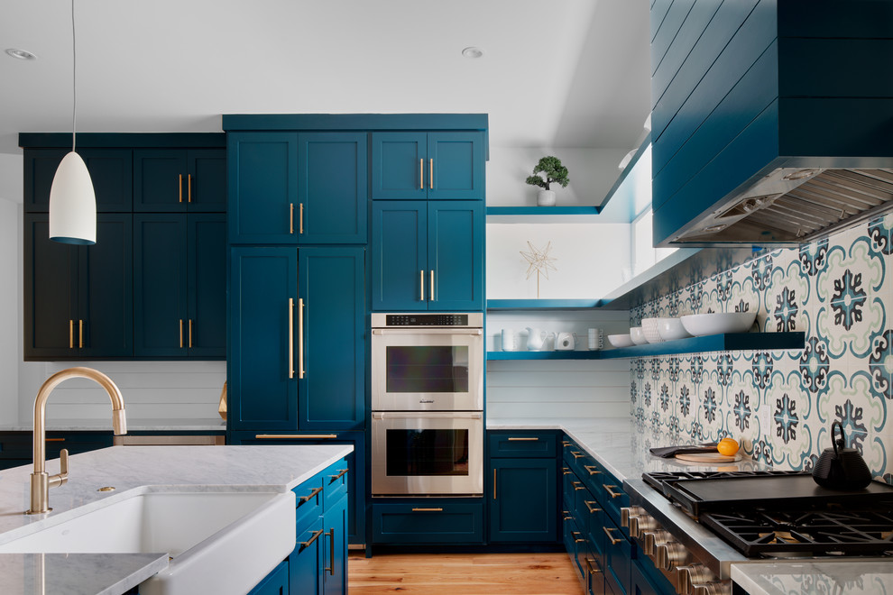 Design ideas for a large contemporary galley kitchen in Austin with a farmhouse sink, shaker cabinets, blue cabinets, marble benchtops, blue splashback, cement tile splashback, panelled appliances, medium hardwood floors, a peninsula and white benchtop.