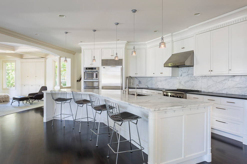 Inspiration for a transitional l-shaped kitchen in Minneapolis with an undermount sink, shaker cabinets, white cabinets, white splashback, marble splashback, stainless steel appliances, dark hardwood floors, with island and black benchtop.