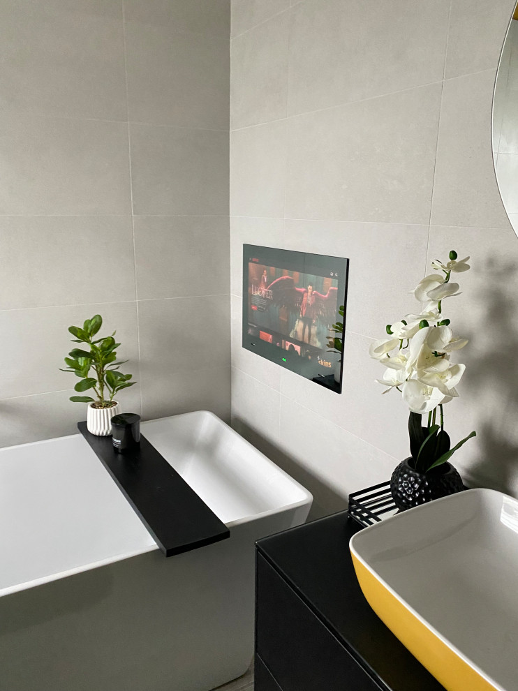 Свежая идея для дизайна: большая детская ванная комната в современном стиле с плоскими фасадами, черными фасадами, инсталляцией, белой плиткой, керамогранитной плиткой, желтыми стенами, полом из ламината, настольной раковиной, стеклянной столешницей, коричневым полом, черной столешницей, отдельно стоящей ванной, открытым душем, душем с распашными дверями, тумбой под одну раковину и подвесной тумбой - отличное фото интерьера