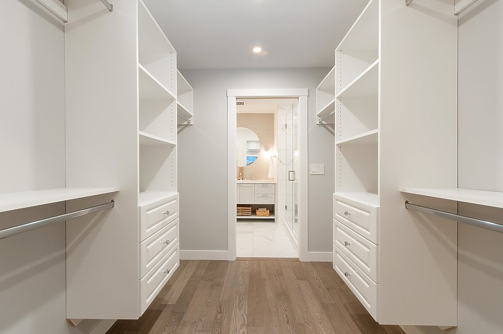 Small beach style gender-neutral walk-in wardrobe in Vancouver with raised-panel cabinets, white cabinets, light hardwood floors and grey floor.