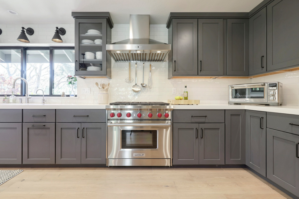 Inspiration for a mid-sized transitional l-shaped laminate floor open concept kitchen remodel with a double-bowl sink, flat-panel cabinets, gray cabinets, quartz countertops, white backsplash, ceramic backsplash, stainless steel appliances, an island and white countertops