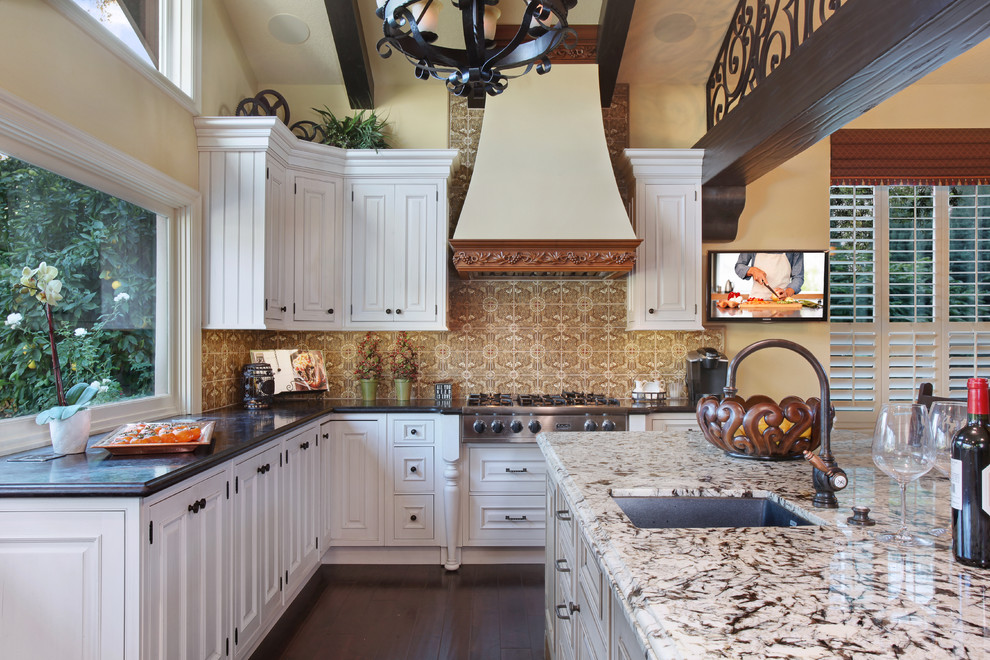 Example of a large classic l-shaped dark wood floor eat-in kitchen design in Orange County with an undermount sink, raised-panel cabinets, white cabinets, brown backsplash, stainless steel appliances, an island, granite countertops and ceramic backsplash