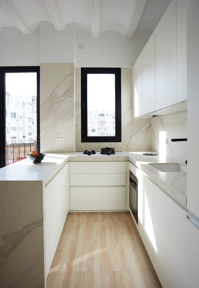 Inspiration for a contemporary u-shaped kitchen in Valencia with an undermount sink, flat-panel cabinets, white cabinets, beige splashback, stainless steel appliances, light hardwood floors, a peninsula, beige floor and beige benchtop.