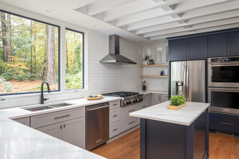 Mid-sized transitional u-shaped medium tone wood floor and brown floor open concept kitchen photo in Raleigh with an undermount sink, recessed-panel cabinets, blue cabinets, quartzite countertops, white backsplash, subway tile backsplash, stainless steel appliances, an island and white countertops