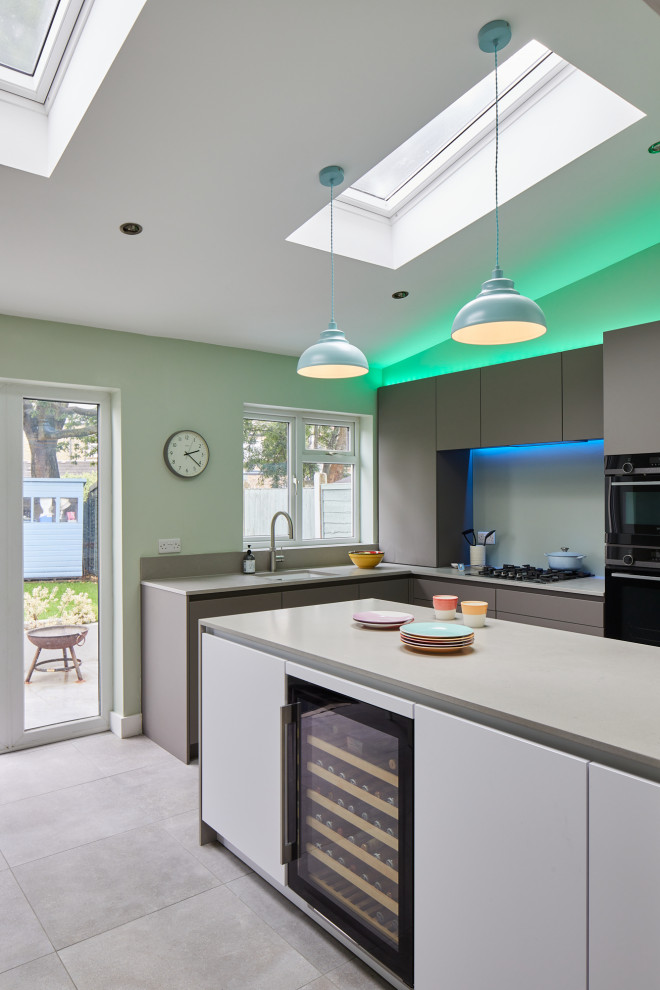 This is an example of a medium sized contemporary l-shaped kitchen/diner in London with a submerged sink, flat-panel cabinets, grey cabinets, engineered stone countertops, glass sheet splashback, stainless steel appliances and an island.