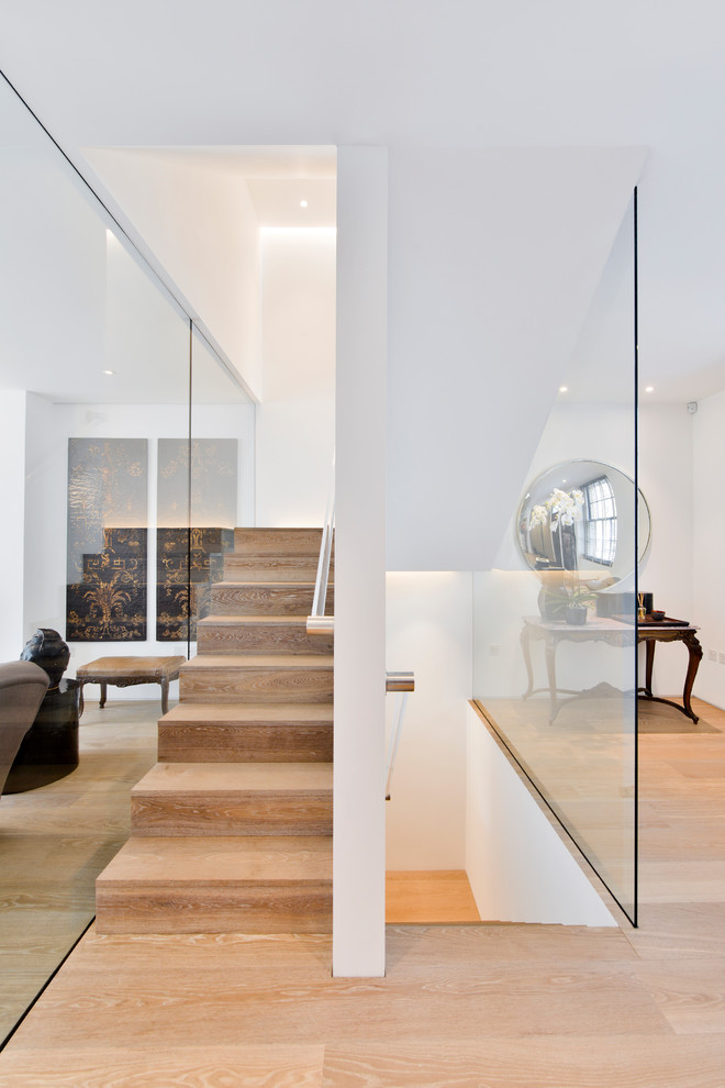 This is an example of a mid-sized modern wood u-shaped staircase in London with wood risers and glass railing.