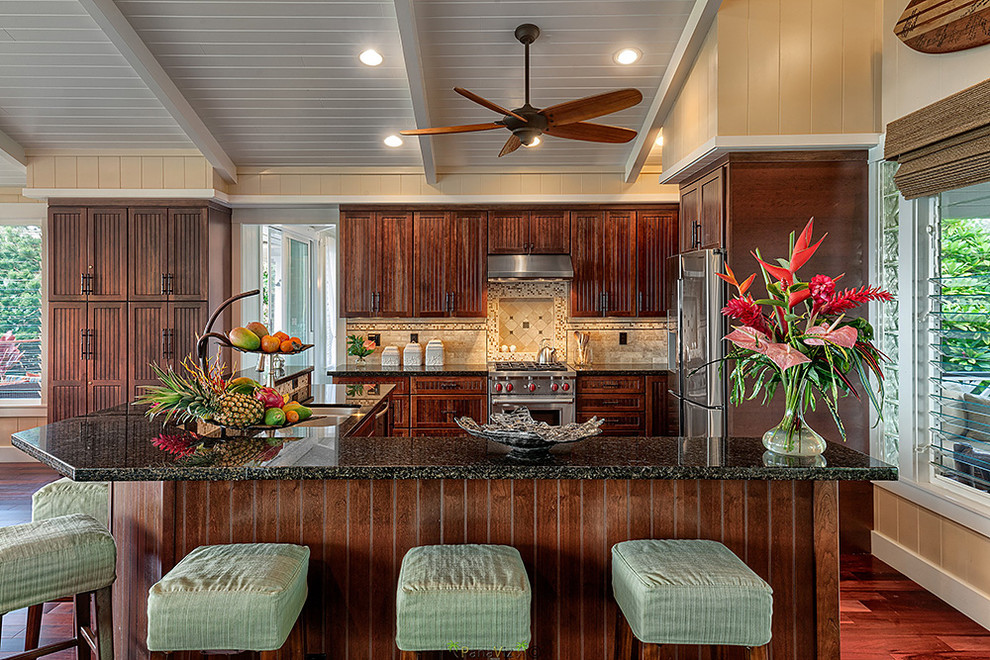 Inspiration for a mid-sized tropical l-shaped open plan kitchen in Hawaii with an undermount sink, flat-panel cabinets, dark wood cabinets, granite benchtops, beige splashback, stone tile splashback, stainless steel appliances, medium hardwood floors and with island.