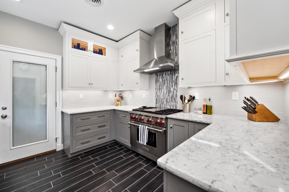 This is an example of a transitional u-shaped kitchen in St Louis with shaker cabinets, grey cabinets, white splashback, subway tile splashback, stainless steel appliances, black floor and white benchtop.