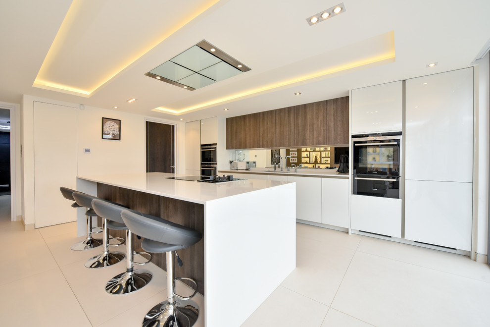 This is an example of a mid-sized modern single-wall open plan kitchen in London with a drop-in sink, glass-front cabinets, white cabinets, quartzite benchtops, metallic splashback, cement tile splashback, black appliances, ceramic floors, with island and white floor.