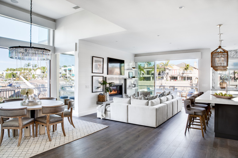 Photo of a large beach style open concept living room in Los Angeles with white walls, medium hardwood floors, a standard fireplace, a stone fireplace surround, a wall-mounted tv and brown floor.