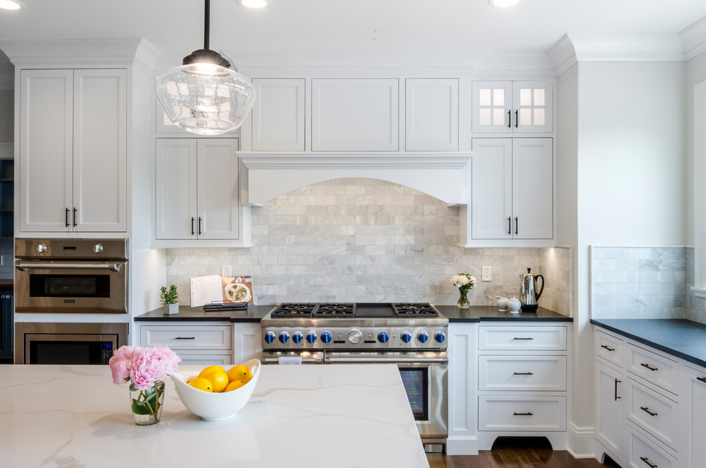 This is an example of a large traditional l-shaped kitchen in Cleveland with shaker cabinets, grey splashback, subway tile splashback, stainless steel appliances, medium hardwood floors, with island, brown floor, white cabinets and quartzite benchtops.