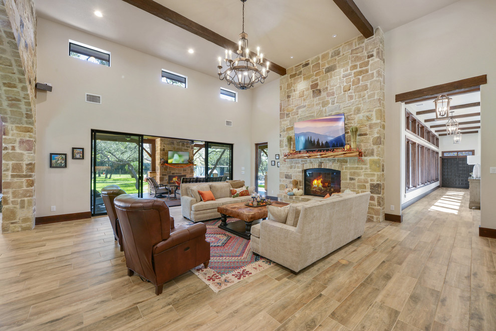Photo of a country open concept living room in Austin with beige walls, ceramic floors, a standard fireplace, a stone fireplace surround, a wall-mounted tv and brown floor.