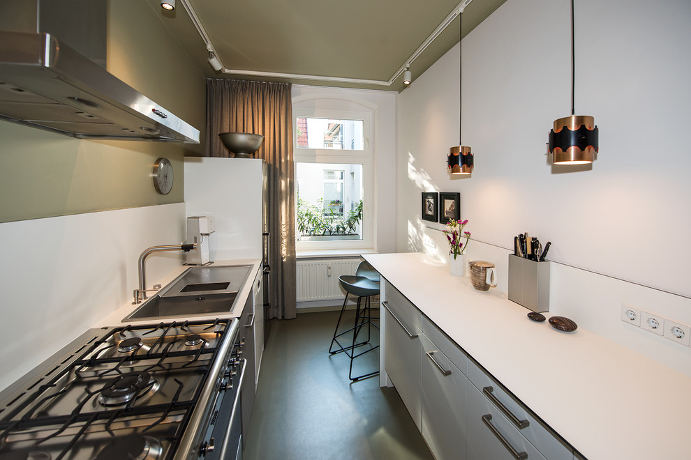 This is an example of a small contemporary galley separate kitchen in Berlin with a drop-in sink, flat-panel cabinets, white cabinets, laminate benchtops, white splashback, stainless steel appliances, linoleum floors, no island, green floor and white benchtop.