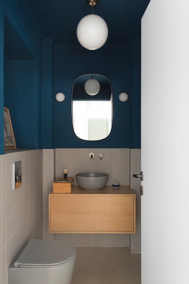 Cette image montre un WC suspendu nordique en bois clair avec un placard à porte affleurante, un carrelage gris, mosaïque, un mur bleu, une vasque, un plan de toilette en bois, un sol beige, un plan de toilette marron et meuble-lavabo suspendu.