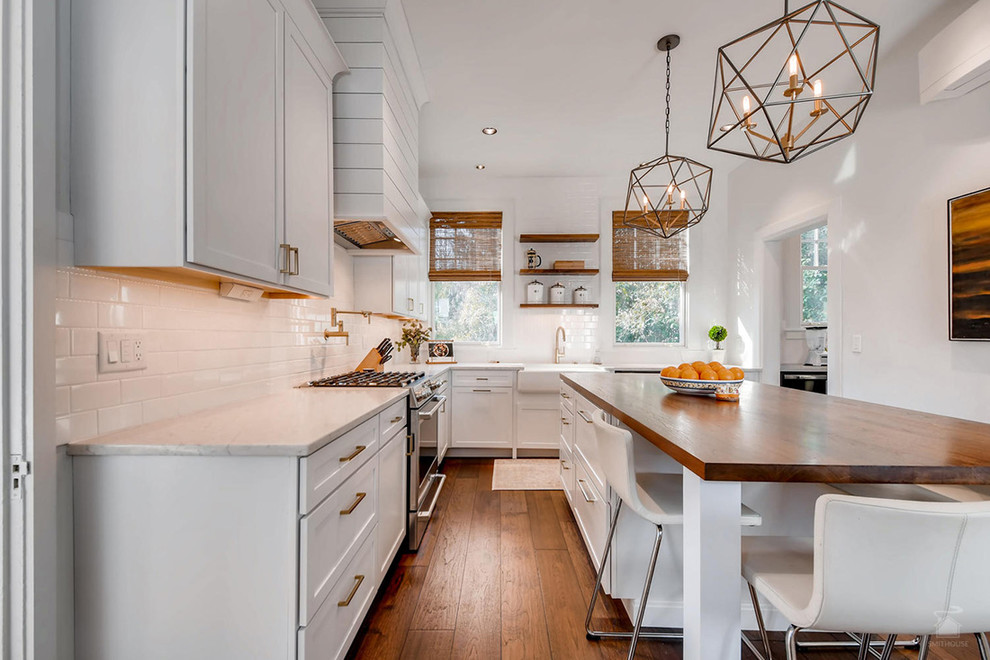 Inspiration for a mid-sized country u-shaped separate kitchen in Baltimore with a farmhouse sink, recessed-panel cabinets, white cabinets, white splashback, subway tile splashback, stainless steel appliances, dark hardwood floors, with island and brown floor.