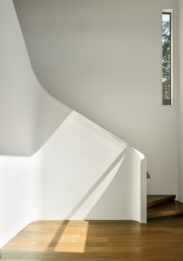 Imagen de escalera curva contemporánea con escalones de madera, barandilla de metal y contrahuellas de metal