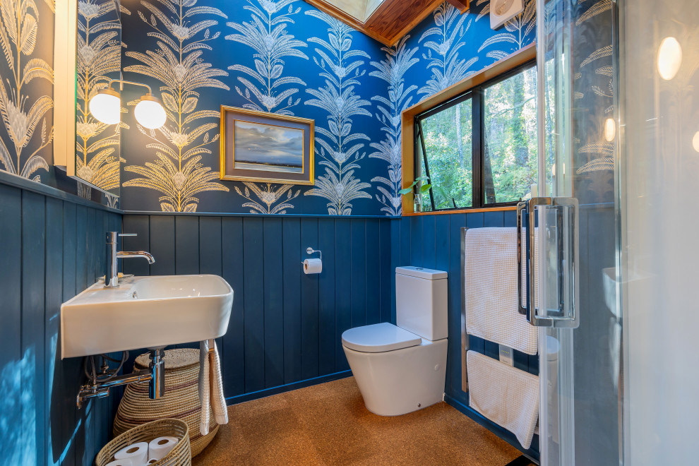 Inspiration for a small eclectic ensuite bathroom in Auckland with white cabinets, a corner shower, a two-piece toilet, blue walls, cork flooring, a wall-mounted sink, brown floors, a sliding door, a single sink, a floating vanity unit and wallpapered walls.
