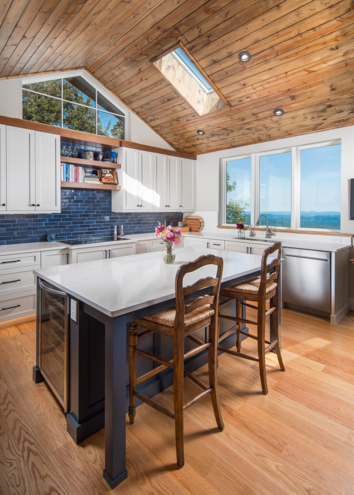 Inspiration for a transitional light wood floor, vaulted ceiling and wood ceiling kitchen remodel with an undermount sink, shaker cabinets, white cabinets, blue backsplash, subway tile backsplash, stainless steel appliances, an island and white countertops