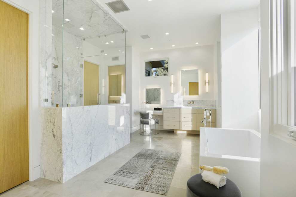 This is an example of a contemporary master bathroom in Los Angeles with flat-panel cabinets, light wood cabinets, a freestanding tub, white tile, marble, white walls, marble benchtops, grey floor, a hinged shower door and white benchtops.