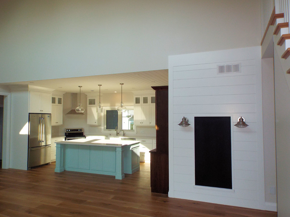 This is an example of a mid-sized beach style u-shaped eat-in kitchen in Other with a farmhouse sink, shaker cabinets, white cabinets, quartz benchtops, white splashback, stainless steel appliances, with island and white benchtop.